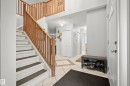 Foyer featuring a two-story entryway, wood balusters, carpeted staircase with dark treads, light tile flooring with a contrasting tile inlay, and a white front entry door with an arched window insert - 15503 62 Street, Edmonton, AB 