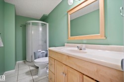 Bathroom featuring a wood-finish vanity with a built-in sink, a framed mirror, a curved shower enclosure, and light-colored tile flooring - 