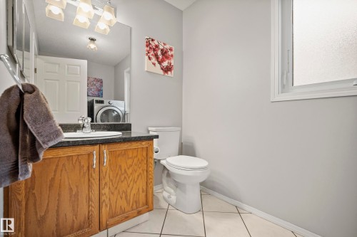 Bathroom featuring a wood-finish vanity with an undermount sink, dark countertop, and tiled flooring - 15503 62 Street, Edmonton, AB 