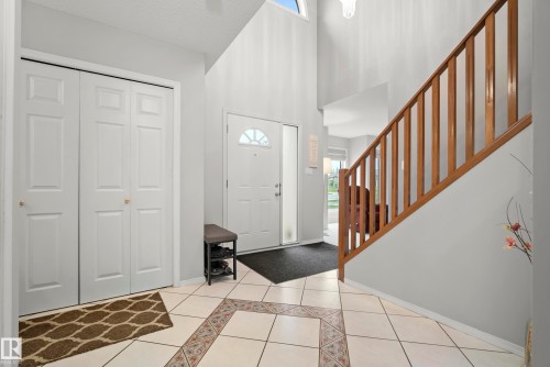 Two-story entryway featuring light-colored tile flooring with decorative inlay, a white front door with an arched window, and a wood staircase with vertical balusters - 15503 62 Street, Edmonton, AB 