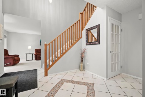 Entryway featuring a natural wood staircase, white tile flooring with decorative inlay, and a multi-pane interior door - 15503 62 Street, Edmonton, AB 