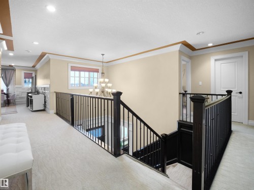 Upper-level landing featuring light-toned carpeting, dark wood-finish newel posts and railings, white panel doors, recessed lighting, and crown molding accents - 2019 Cameron Ravine Way Nw, Edmonton, AB 