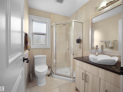 Bathroom featuring a corner glass-enclosed shower, a contemporary vessel sink on a dark countertop, a light wood-finish vanity with cabinet storage, and light-toned tile flooring - 2019 Cameron Ravine Way Nw, Edmonton, AB 