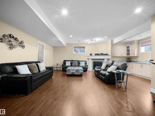 Spacious entertainment area featuring wood-finish flooring, a built-in wet bar with cabinetry, a fireplace with a mantel, recessed lighting, and a sliding door - 2019 Cameron Ravine Way Nw, Edmonton, AB 