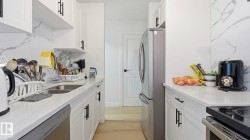 Galley kitchen featuring white cabinetry with black hardware, light-toned countertops, and a white marble-look backsplash - 