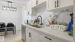Modern kitchen featuring white cabinetry with black hardware, a stainless steel double basin sink, a dark finish gooseneck faucet, and a quartz countertop - 