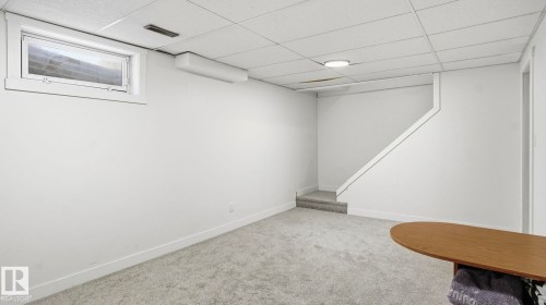 Finished lower-level space featuring light gray carpeting, white painted walls, a drop ceiling with recessed lighting, a built-in staircase, and an egress window - 20C Callingwood Court, Edmonton, AB - Indoor Photo Showing Other Room