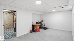 Finished basement room featuring light gray carpeting, white walls, and a drop ceiling with integrated lighting - 