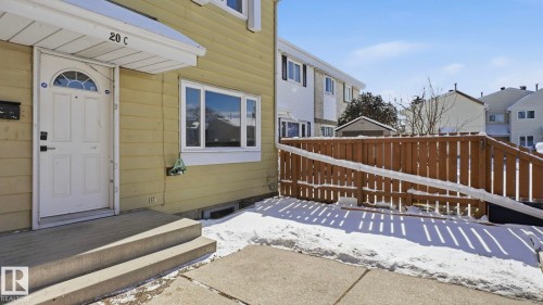 Exterior entry featuring a white paneled door with an arched glass insert, concrete steps, a protective overhang, and vinyl siding - 20C Callingwood Court, Edmonton, AB - Outdoor With Exterior