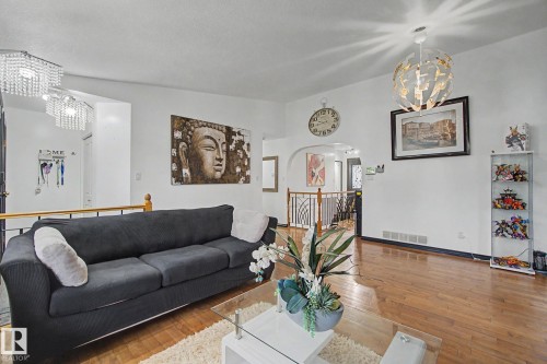 Spacious living area featuring wood-finish flooring, white walls, and a distinctive decorative chandelier - 242 Northmount Drive, Wetaskiwin, AB 