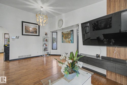 Spacious living area featuring wood-finish flooring, a contemporary chandelier, and a feature wall with integrated media console - 242 Northmount Drive, Wetaskiwin, AB 