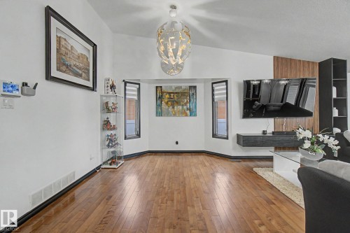 Living area featuring wood-finish flooring, vaulted ceilings, a geometric chandelier, bay windows, and a modern media wall with vertical wood paneling - 242 Northmount Drive, Wetaskiwin, AB 