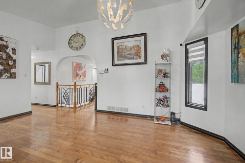 Hardwood-finish flooring extends throughout this expansive area, featuring an arched doorway, black baseboards, and a contemporary chandelier - 242 Northmount Drive, Wetaskiwin, AB 