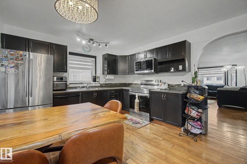Modern kitchen featuring dark cabinetry, stainless steel appliances, and wood-finish flooring - 242 Northmount Drive, Wetaskiwin, AB 