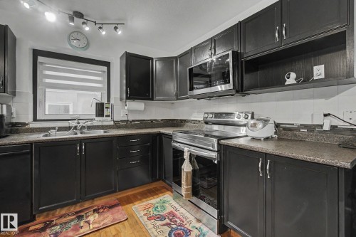 Kitchen featuring dark cabinetry, stainless steel appliances, a double basin sink, and wood-finish flooring - 242 Northmount Drive, Wetaskiwin, AB 
