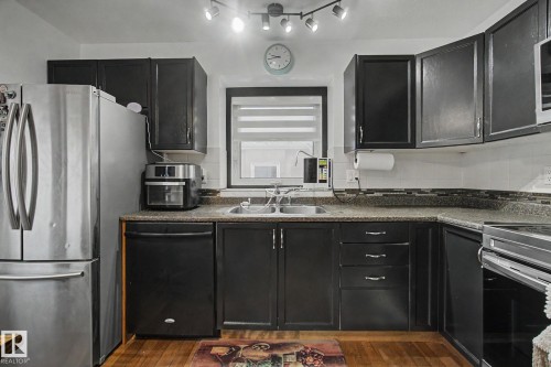 Kitchen featuring dark cabinetry, light-colored countertops, stainless steel refrigerator, and wood-finish flooring - 242 Northmount Drive, Wetaskiwin, AB 