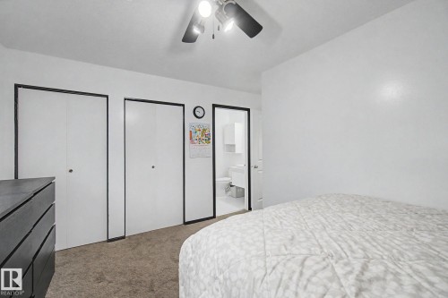 Bedroom featuring a ceiling fan, plush carpet, two bi-fold closet doors, and an entry to an additional space - 242 Northmount Drive, Wetaskiwin, AB 