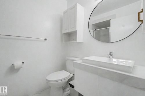 Contemporary bathroom featuring a rectangular vessel sink, white vanity, round wall mirror, wall-mounted cabinetry, and chrome fixtures - 242 Northmount Drive, Wetaskiwin, AB 