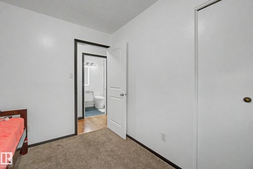 Carpeted room with white walls and dark trim, featuring a white door and a closet with a brass-toned knob - 242 Northmount Drive, Wetaskiwin, AB 