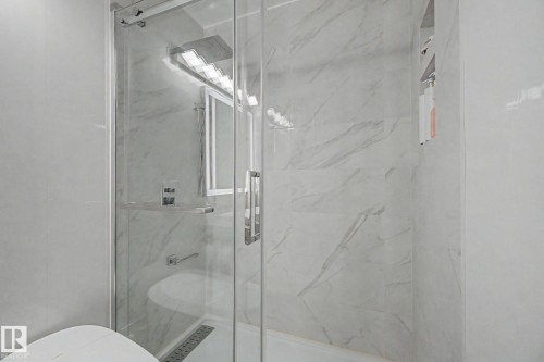 Glass-enclosed shower featuring large format tile walls with subtle veining, a built-in shower niche, a linear drain, and brushed nickel fixtures - 242 Northmount Drive, Wetaskiwin, AB 