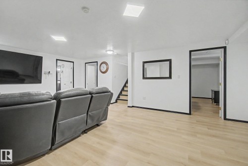 Spacious entertainment area featuring light wood-finish flooring, white walls, and contrasting black trim - 242 Northmount Drive, Wetaskiwin, AB 