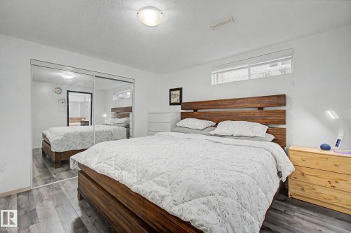 Bedroom featuring wood-finish flooring, a wood slatted headboard, and mirrored closet doors - 242 Northmount Drive, Wetaskiwin, AB 