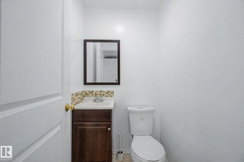 Bathroom featuring a wood-finish vanity with a white countertop and drop-in sink, mosaic tile backsplash, framed mirror, and a white toilet - 242 Northmount Drive, Wetaskiwin, AB 