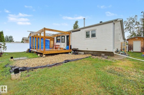 Rear exterior featuring a wood deck with an open pergola frame, white vinyl siding, a gravel area, a small shed, and a privacy fence - 242 Northmount Drive, Wetaskiwin, AB 