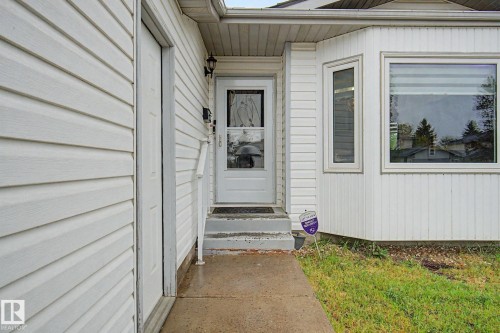 White vinyl siding exterior with an entry door featuring decorative glass and a storm door - 242 Northmount Drive, Wetaskiwin, AB 