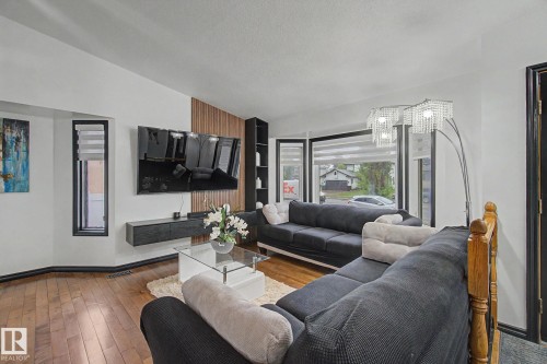 Living area with wood-finish flooring, a contemporary wall-mounted media console, and a contrasting vertical wood-panel accent wall - 242 Northmount Drive, Wetaskiwin, AB 