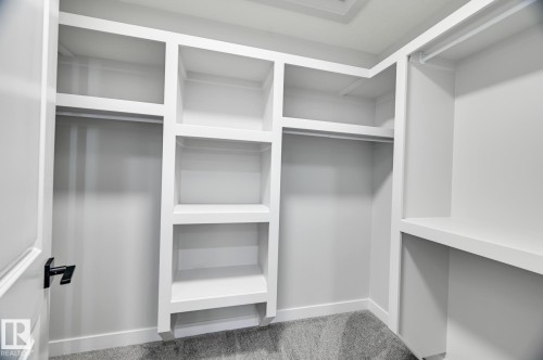 Walk-in closet featuring built-in white shelving, multiple hanging rods, and gray carpet flooring - 54 Chartres Close, St. Albert, AB - Indoor With Storage