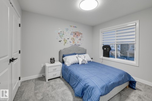 Carpeted room featuring a double-pane window with horizontal blinds, a ceiling-mounted light fixture, white interior doors with black hardware, and an upholstered headboard - 54 Chartres Close, St. Albert, AB - Indoor Photo Showing Bedroom