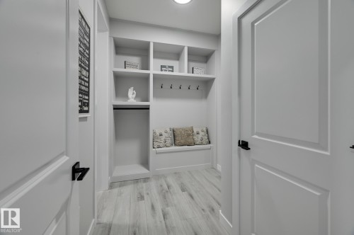 Entryway featuring wood-finish flooring, built-in storage with cubbies, an integrated bench, and black hardware on white panel doors - 54 Chartres Close, St. Albert, AB - Indoor