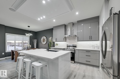 Contemporary kitchen featuring an oversized island with countertop seating, glossy gray cabinetry, stainless steel appliances, and wood-finish flooring - 54 Chartres Close, St. Albert, AB - Indoor Photo Showing Kitchen With Upgraded Kitchen