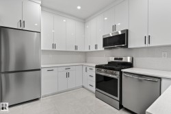 Contemporary kitchen featuring white flat-panel cabinetry with matte black hardware, stainless steel appliances, light-toned countertops, and coordinating backsplash - 