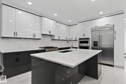 Modern kitchen featuring a large central island with an undermount sink, stainless steel appliances, two-tone cabinetry, recessed lighting, and light-toned tile flooring - 