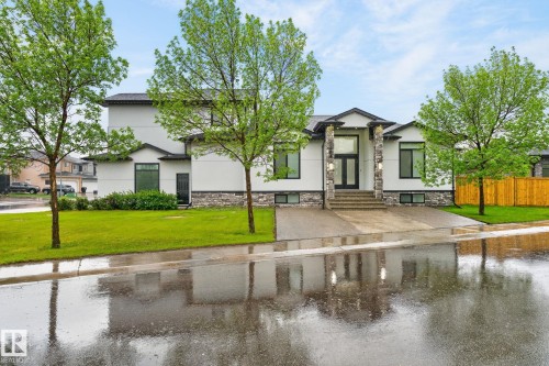 Contemporary exterior featuring white siding and stone accents, a prominent entryway with double doors, dark-framed windows, a concrete driveway, and a manicured lawn - 7304 164 Avenue, Edmonton, AB - Outdoor With Facade