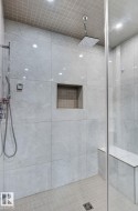 Spacious walk-in shower featuring large format wall tiles, a built-in shower bench, and a rain shower head - 