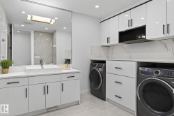 Integrated laundry and vanity space featuring a vessel sink, quartz countertops, white cabinetry with matte black hardware, and an expansive mirror - 