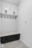 Built-in entryway storage featuring a white countertop with grey veining, black base cabinetry, and overhead white cabinetry with black hardware - 