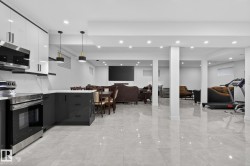 Open-concept lower level featuring a contemporary kitchen with stainless steel appliances, sleek dark and white cabinetry, and a light-colored countertop - 