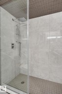 Glass-enclosed shower with large format light gray wall tiles, a ceiling-mounted rainfall showerhead, and a hand-held shower fixture - 