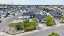 Contemporary residence featuring a paved driveway, stone facade accents, a dark shingle roof, and mature landscaping - 