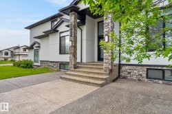 Modern architectural exterior featuring white stucco siding, dark trim accents, and a stone veneer foundation - 