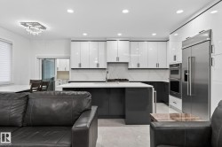 Modern kitchen featuring two-tone cabinetry with white upper and dark lower cabinets, a large center island with integrated sink, stainless steel appliances, and tile flooring - 