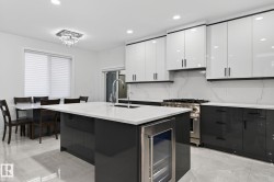 Modern kitchen featuring a large central island with a built-in beverage cooler, white countertops, and a stainless steel sink - 