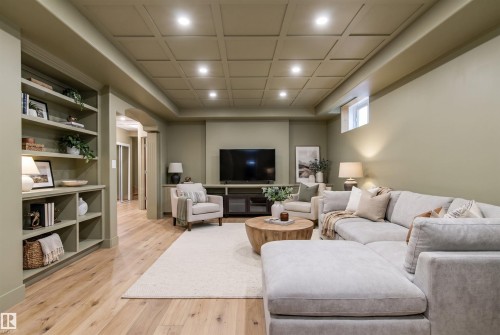 Open living space featuring a coffered ceiling with recessed lighting, built-in shelving, wood-finish flooring, and an arched entryway - 703 107A Street, Edmonton, AB 