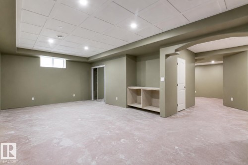 Spacious room featuring neutral carpeting, recessed lighting, drop ceiling, a built-in storage unit, and a window - 703 107A Street, Edmonton, AB 