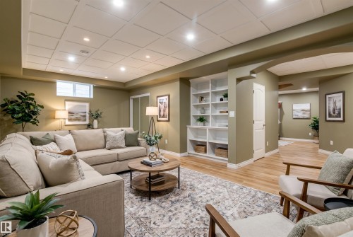 Spacious living area featuring coffered ceilings with recessed lighting, built-in shelving, wood-finish flooring, and a window - 703 107A Street, Edmonton, AB 