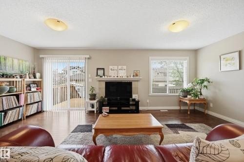 Spacious living area featuring rich wood-finish flooring, a contemporary fireplace with a white mantel, and a large window with blinds - 1111 176 Street, Edmonton, AB 